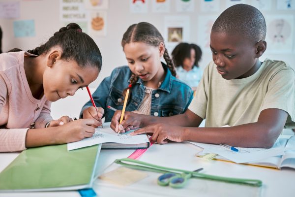 A group of adolescent students are sitting around a table writing.