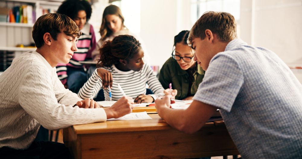 A group of teens sit around a table engaged in literacy work.